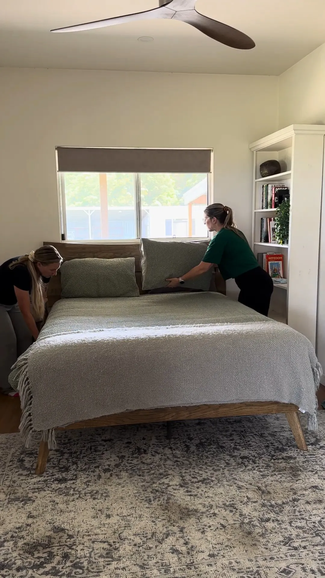 Two TLB cleaners presenting the cushions on a freshly made bed in a holiday home bedroom