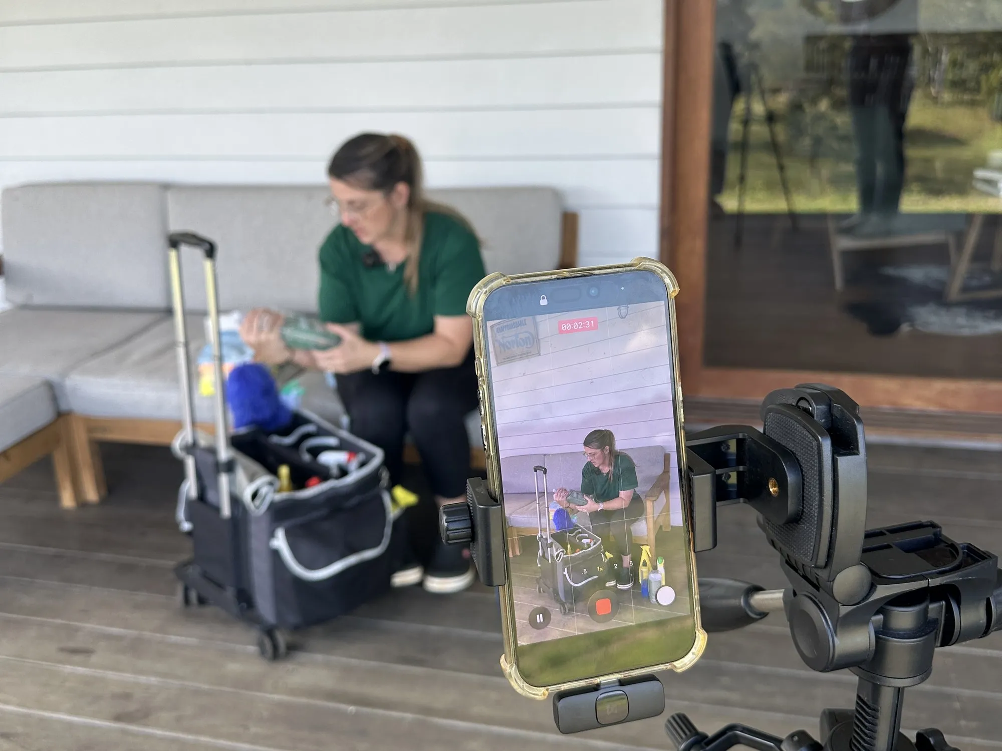 A cleaner sorting supplies from her trolley on a deck, recorded on a phone on a tripod