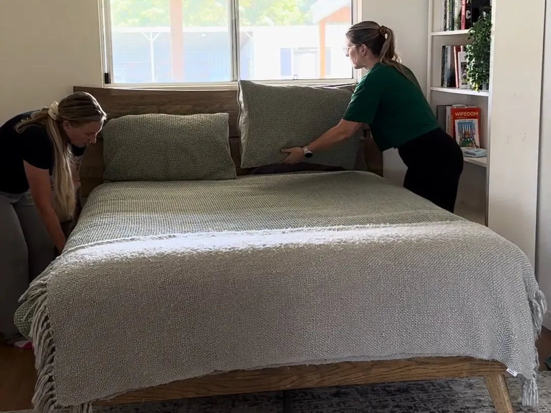 Two cleaners presenting the cushions on a freshly made bed