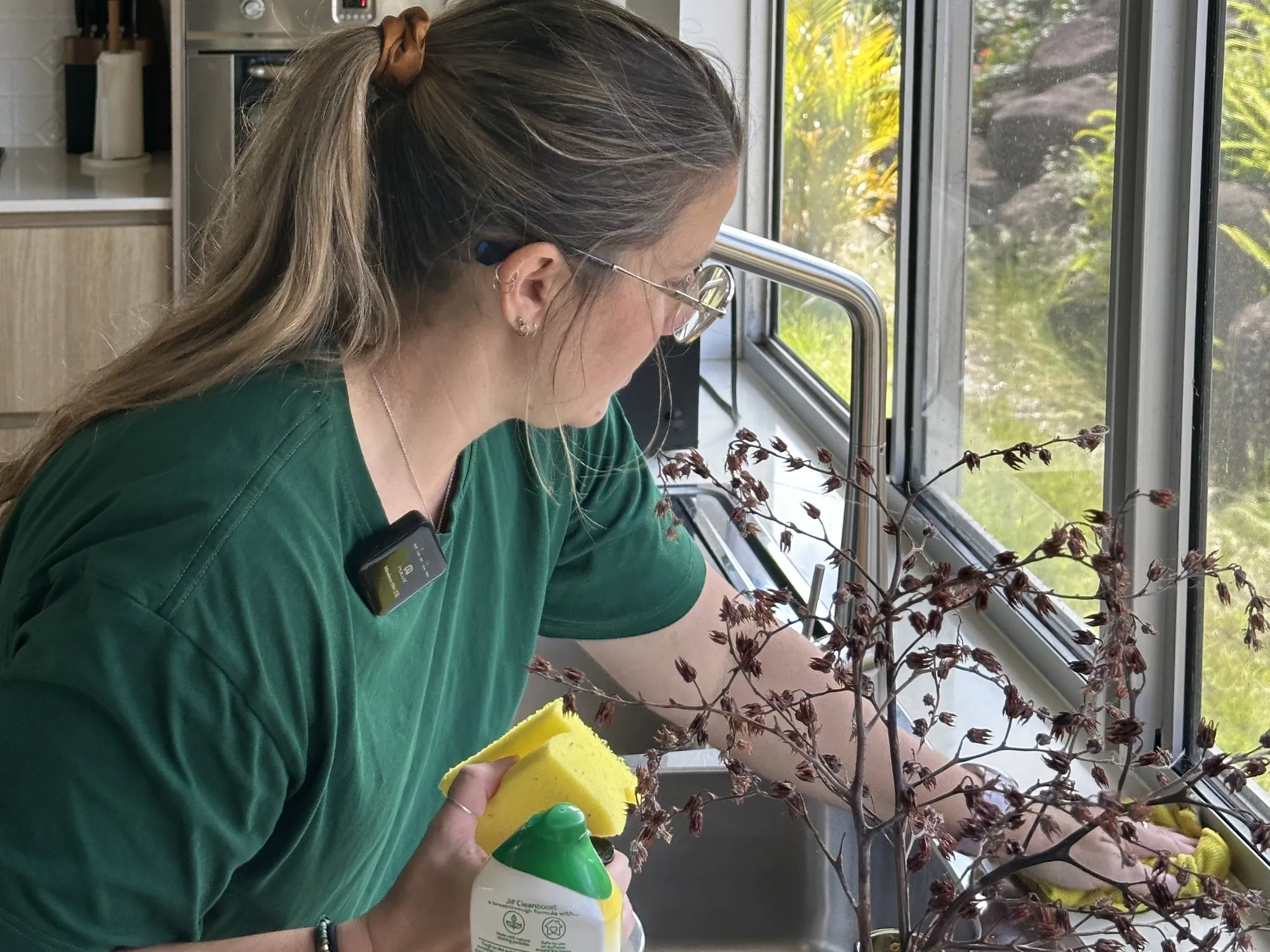 A cleaner wiping down the kitchen window sill with a sponge and spray