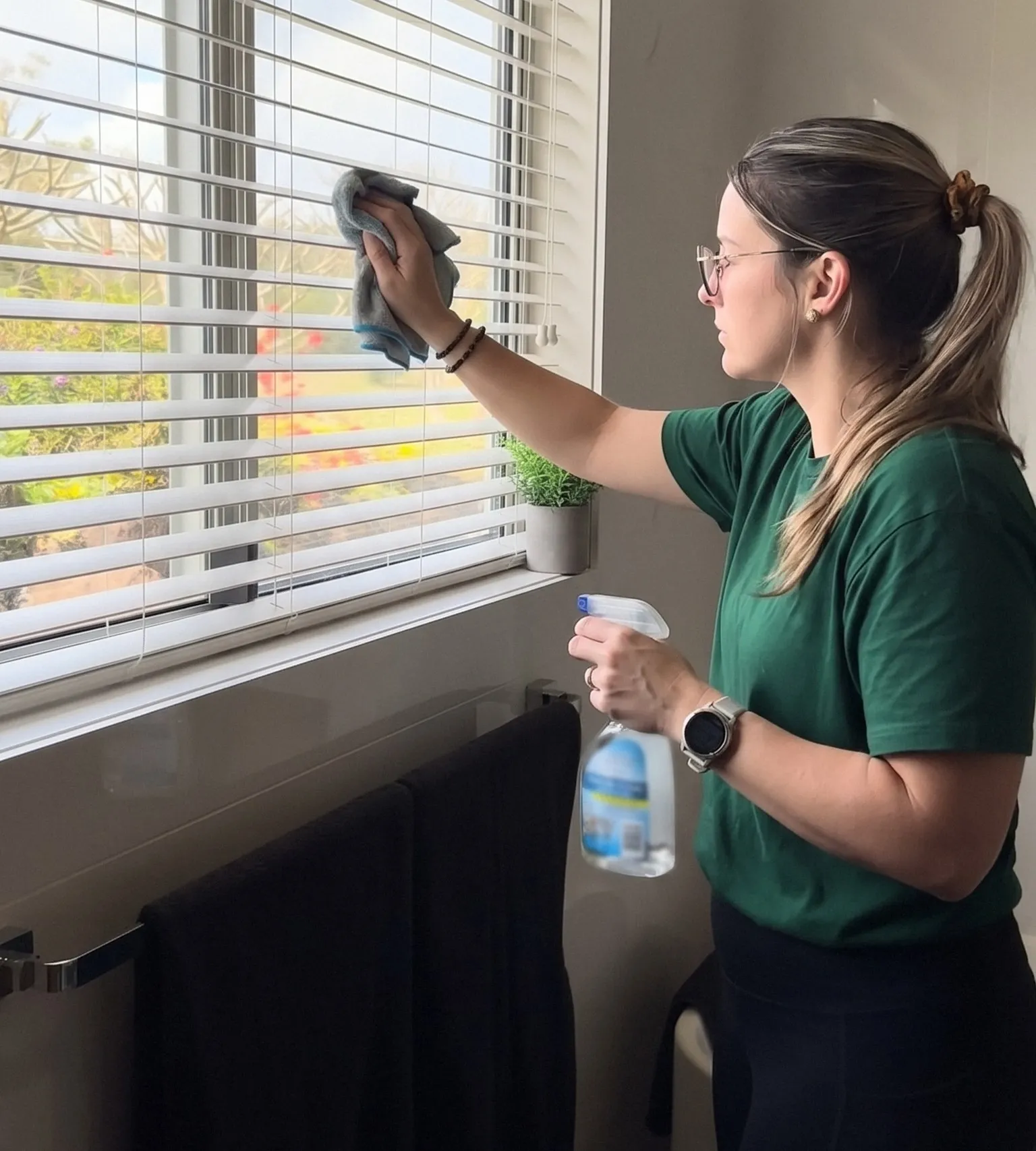 A cleaner wiping the slats of a white venetian blind with a microfibre cloth