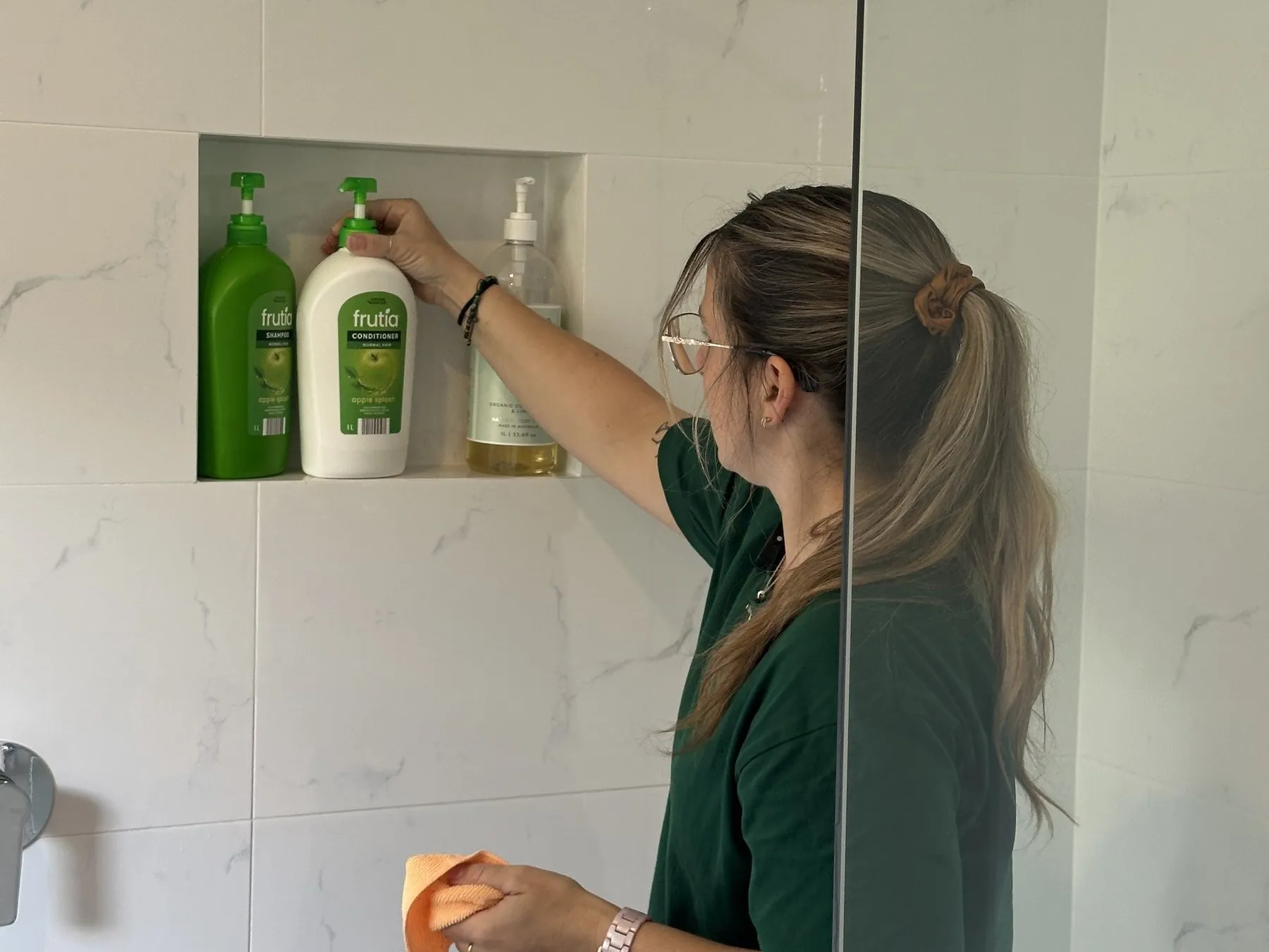 A cleaner straightening the bottles in a tiled shower niche