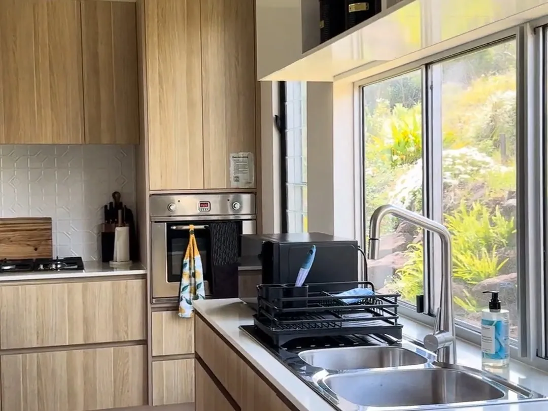 A tidy, sunlit kitchen with timber cabinets and a garden window