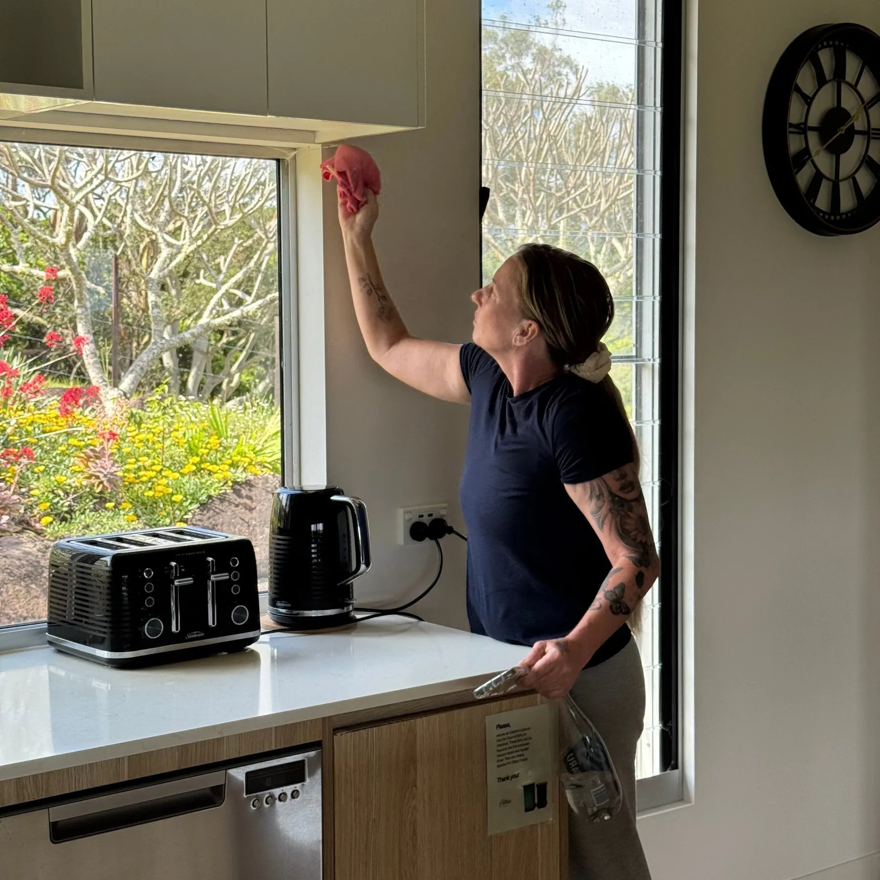 Cleaner reaching up with a cloth to wipe down a kitchen window frame