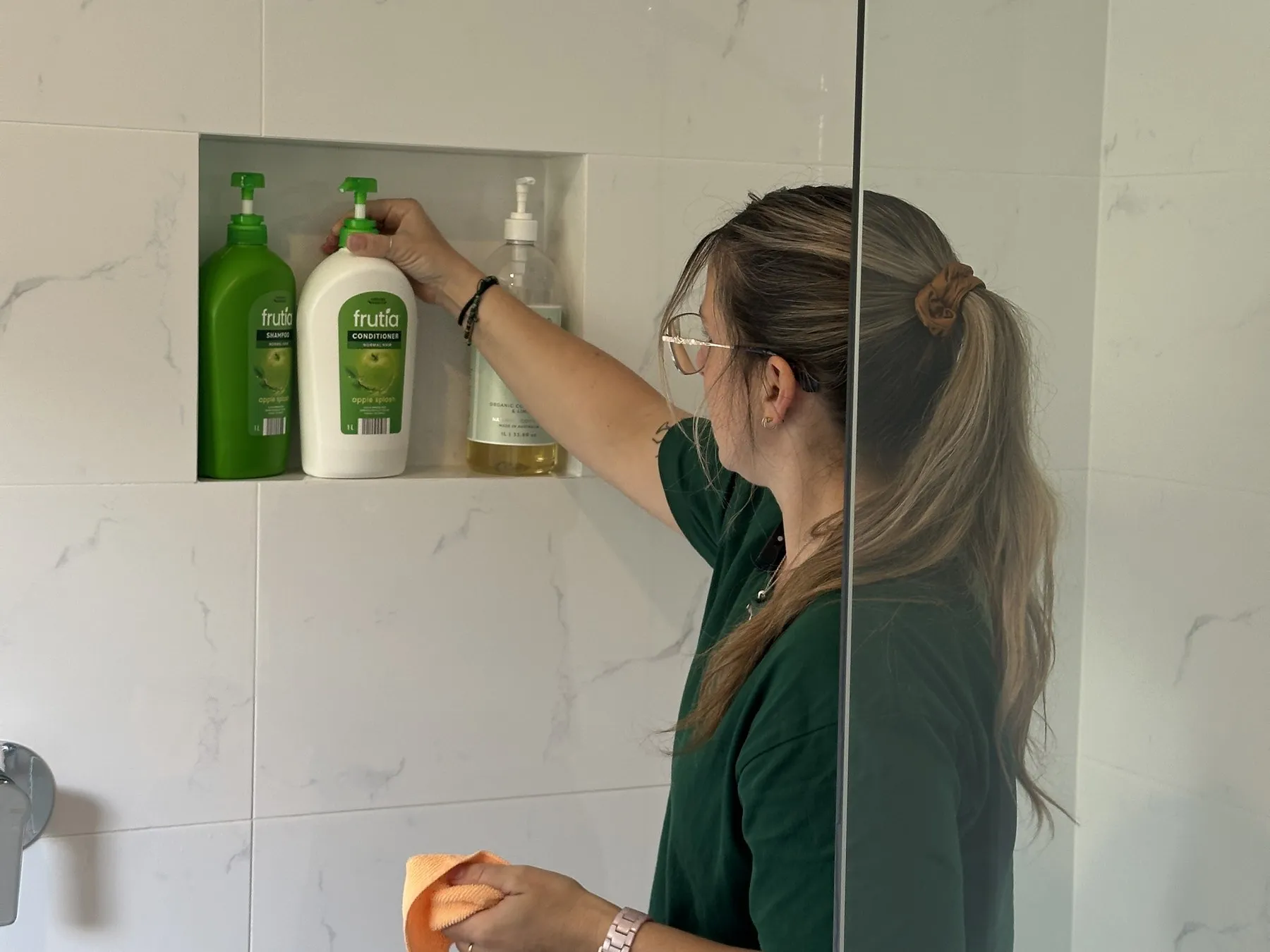 A TLB cleaner straightening the bottles in a tiled shower niche