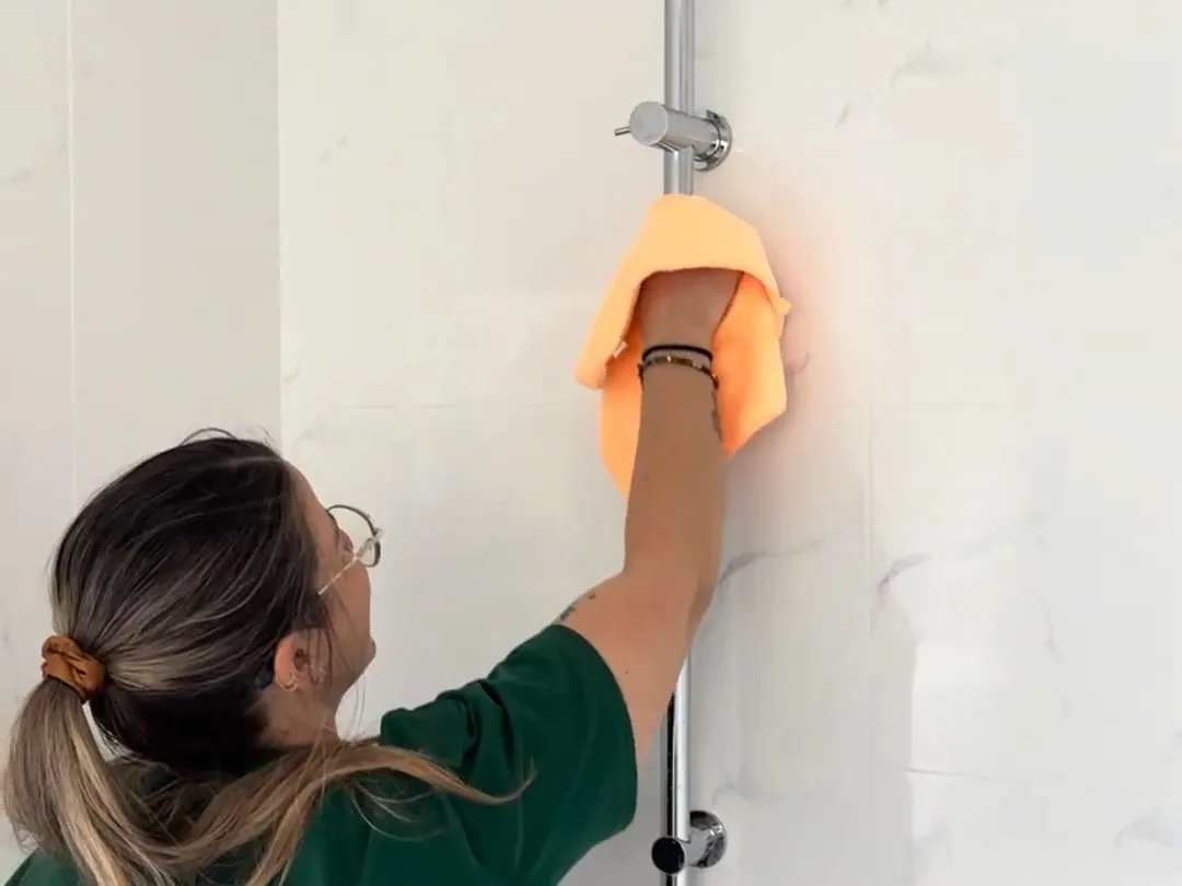 A TLB cleaner wiping down the rail and fittings of a walk-in shower