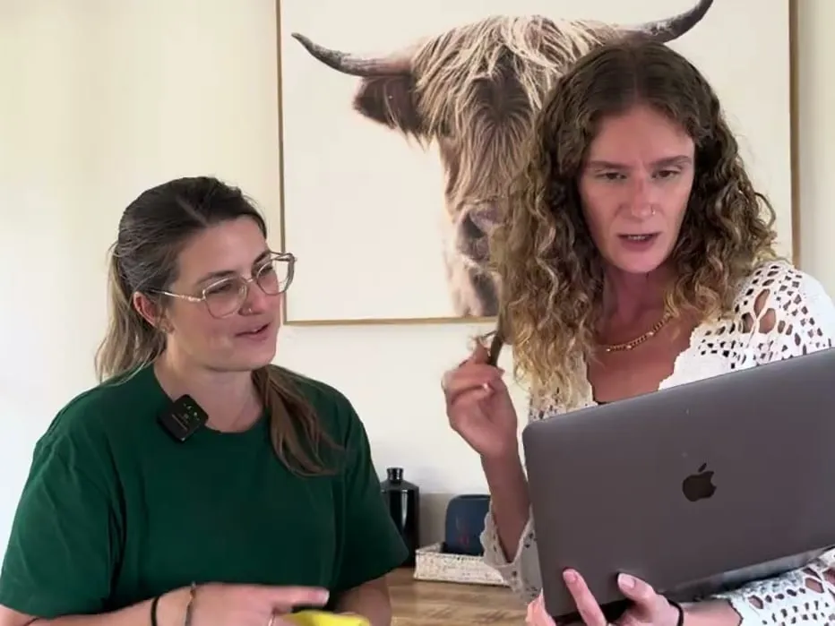 Two women looking over a laptop together in a living room, one in the green TLB uniform